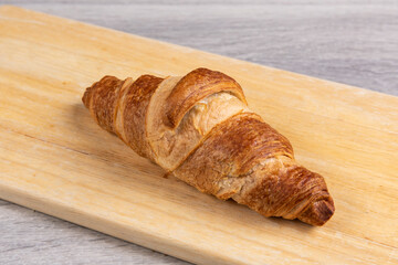 A single French croissant on a wooden board