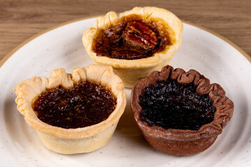 A plate of assorted artisanal butter tarts including pecan and chocolate with rough crusts