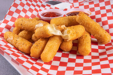 A plate of deep fried breaded mozzarella sticks with dipping sauce on red checkered paper