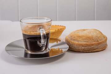A glass cup of coffee expresso with Italian pastries on a white table