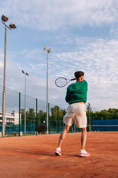 Tennis player serves on a clay court under a cloudy sky