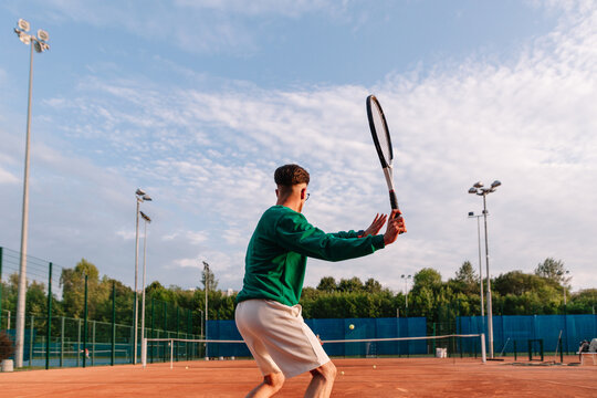 Tennis player practices on a clay court during a sunny afternoon