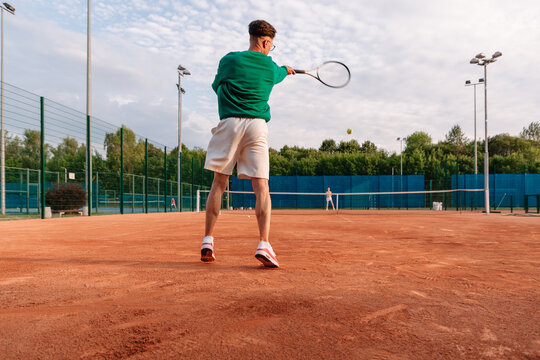 Tennis player practices on clay court during a sunny afternoon