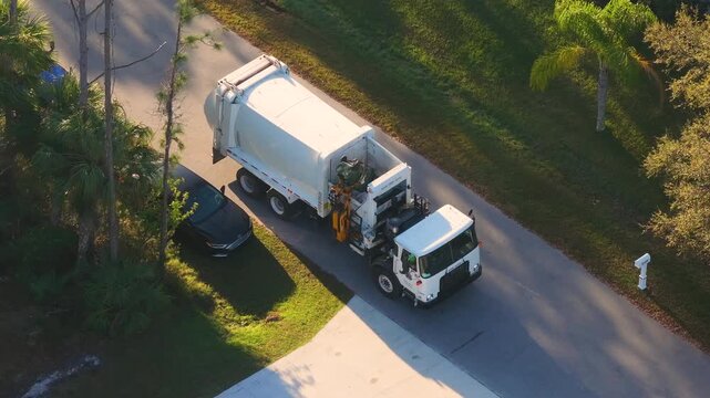 American garbage truck picking up trash bins on rural street side.