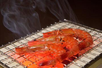 煙り立ち昇る七輪で海老を焼く