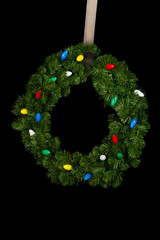 Green festive fir branch holiday wreath decorated with colorful lights isolated on black
