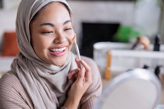 Woman in hijab smiles to apply blush on cheeks