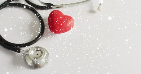 Showing black stethoscope looping left, red heart resting near chest piece on white tabletop, bokeh