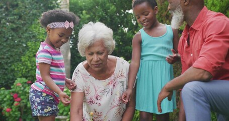 Planting two seniors and two children tending seedling in backyard soil patch, floral blouse © vectorfusionart
