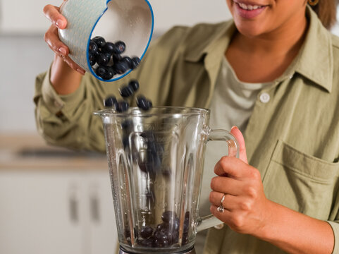 Woman pouring blueberries into blender
