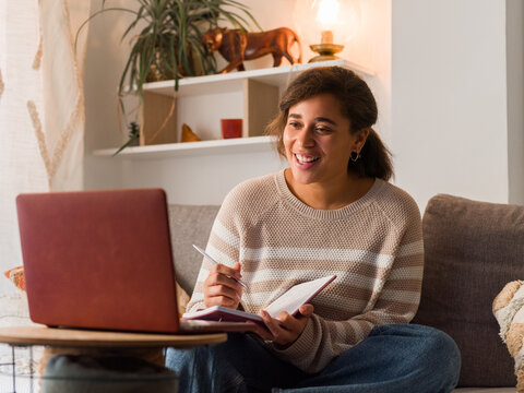 Young Woman Enjoys Online Class While Taking Notes at Home