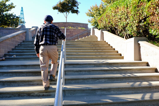 older man walks holding handrail