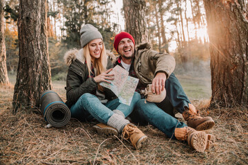 Travel couple camping with map having fun in the forest. Concept of trekking, adventure and seasonal vacation.