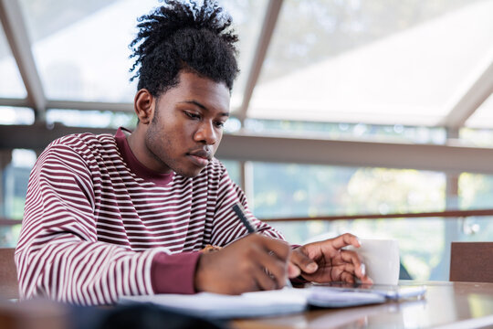 Young man studies with coffee, pen, and notebook.