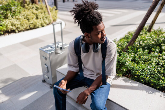 Traveler with luggage sits, looks away, and holds phone.