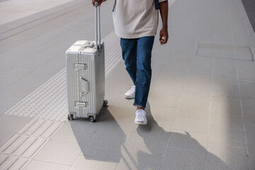 Traveler pulls silver suitcase on textured sidewalk.