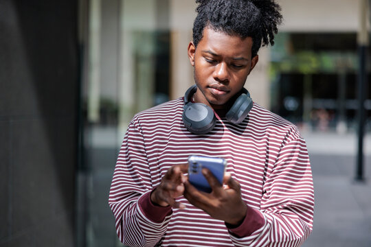 Young man with headphones using a smartphone outdoors.