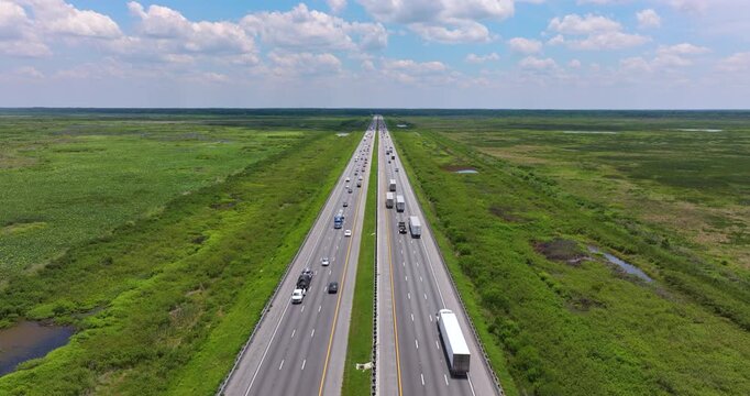 Straight section of interstate highway in Florida wetland zone, bordered by grassy water channels and driving traffic.