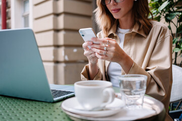 Woman using phone at outdoor cafe with laptop and coffee