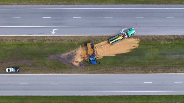 Traffic accident involving overturned semi-truck leaking sand on highway. Tow crew on site.