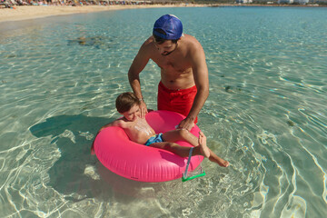 Father Applying Sunscreen to Son in Floating Ring