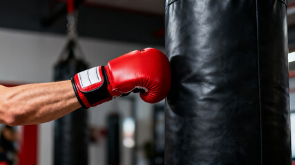 Close-up of a boxer hitting a heavy punching bag with a red glove in a gym.
