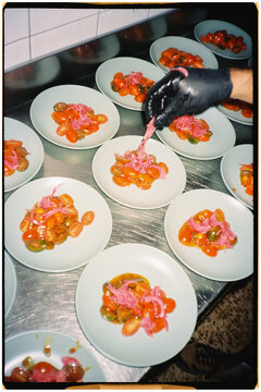 Chef's hand plating tomato and onion appetizers at a kitchen counter