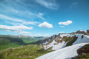 Scenic view from top to multi-tiered dale with melting snows and streams of melt water under lush clouds in blue sky. Colorful landscape with green wide valley. Changeable weather in high mountains. © Daniil