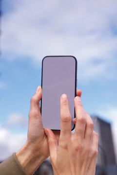 Hand of partial woman using and typing cellphone on cloudy sky back