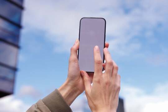 Hand of cropped woman using smartphone near skyscraper on cloudy sky