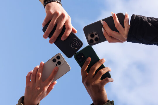 Partial bottom of hands holding various mobile phones on cloudy sky