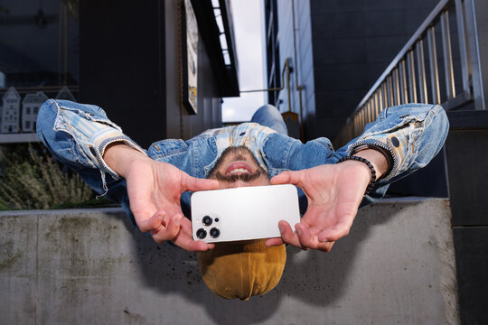 Man in upside down pose on concrete block taking photo on smartphone