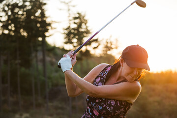 Candid golf swing at sunset by a woman golfer wearing cap and glove