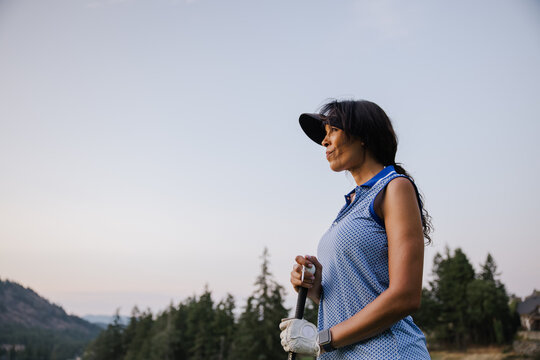 Candid outdoor golfer woman in blue polo with clubs, focused at dusk