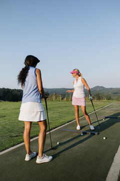 Candid scene of two women practicing golf on a sunny driving range