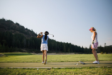 Women practicing golf on driving range with coach friend watching
