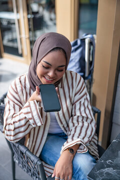 Young woman using voice command on smartphone at outdoor cafe
