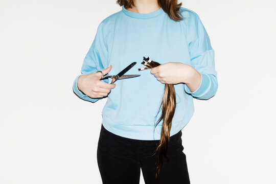 Conceptual image of person cutting long hair with silver scissors