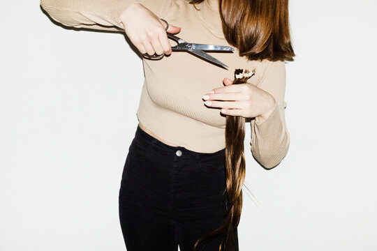Conceptual image of person cutting long hair with silver scissors