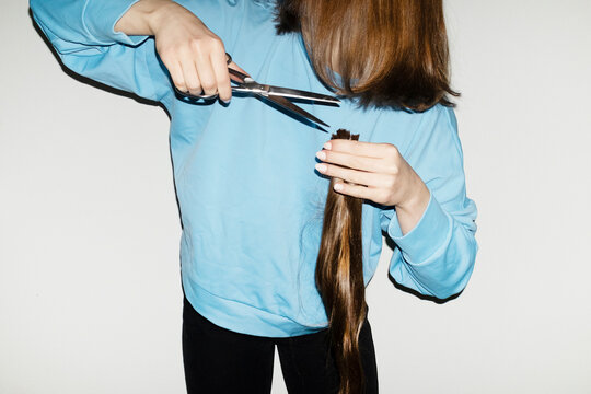 Conceptual image of person cutting long hair with silver scissors