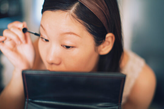 Woman Concentrates on Applying Mascara in Front of a Mirror.