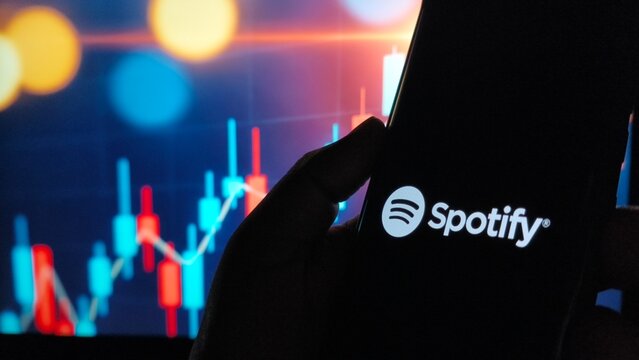 Spotify logo on phone screen with stock market graph background