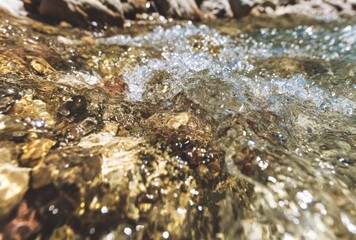 Close-up of flowing water cascading over smooth, colorful rocks in a shallow stream