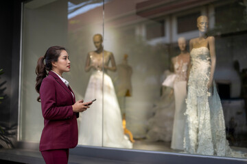 Woman window shopping wedding dresses with smartphone