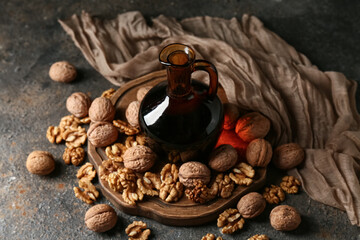 Jug of fresh walnut oil and wooden board with nuts on dark background