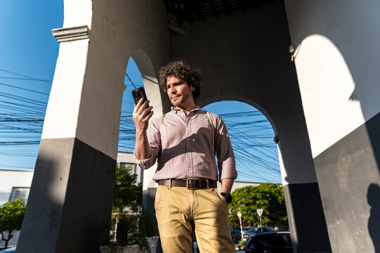 Digital nomad checking phone under sunny archway