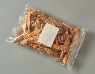 dried curd chillies in clear plastic packet isolated neutral gray background, sun-dried salted peppers visible through transparent glossy packaging with blank white rectangular label, top view