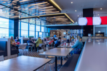 Fototapeta premium Blurred interior of a modern restaurant and food court with people dining inside. Defocused background for cafe and food service concepts.