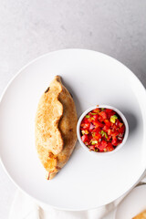 Overhead view of baked empanadas with pico de gallo on a white plate, top view of empanadas and salsa, bolivian salte&ntilde;a with chopped tomato sauce