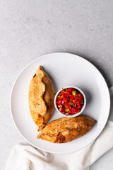 Overhead view of baked empanadas with pico de gallo on a white plate, top view of empanadas and salsa, bolivian salte&ntilde;a with chopped tomato sauce